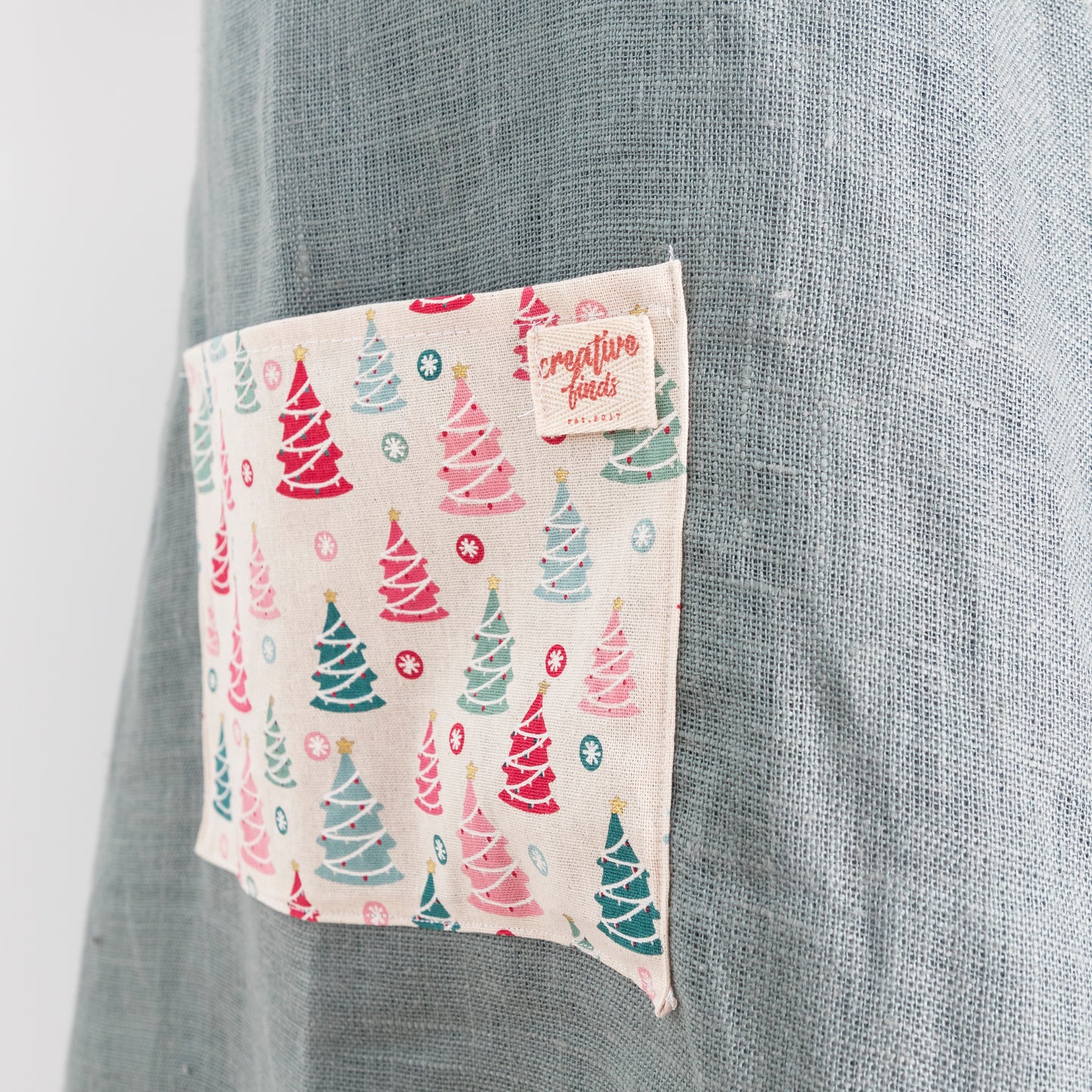 close up of pocket on green linen apron with christmas fabric on pocket and frill