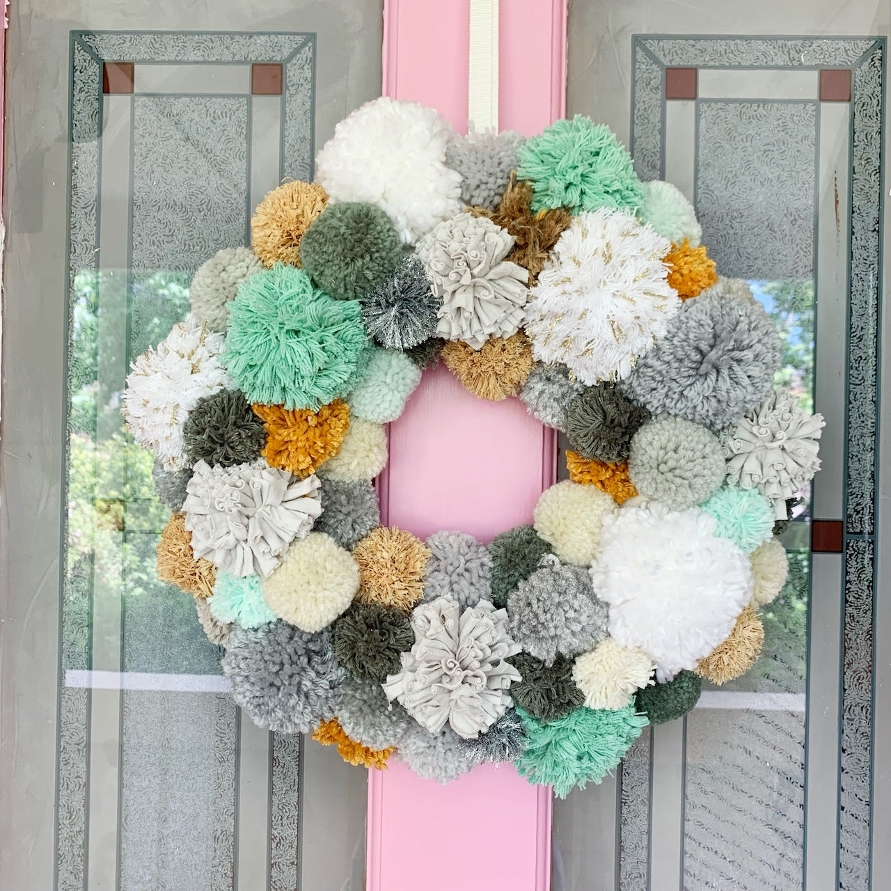 Green PomPom Wreath hanging on pink front door