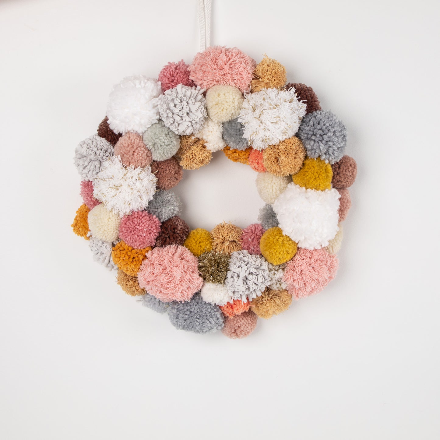 earth warm - pinks PomPom Wreath hanging on white background