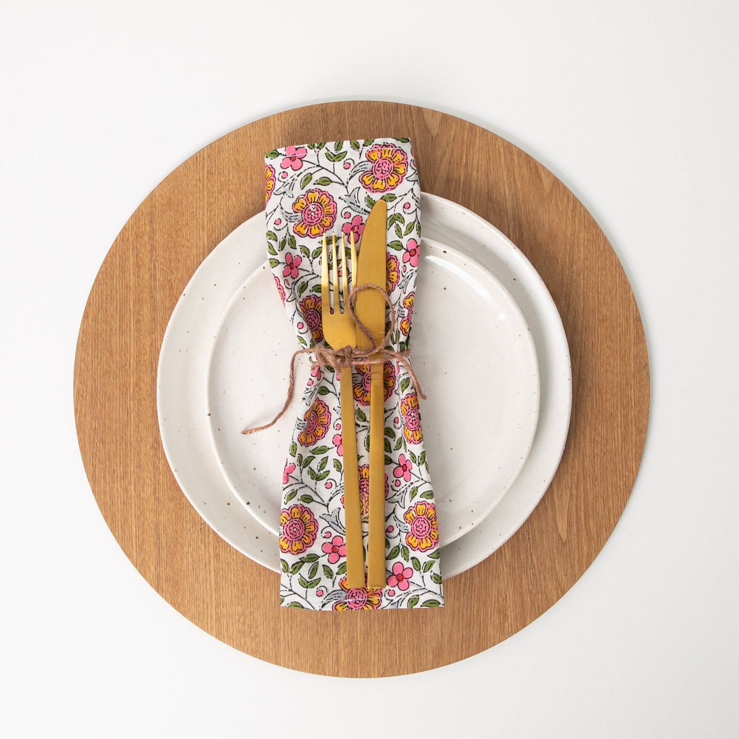 floral napkin tied with string sitting on white plate with gold cutlery