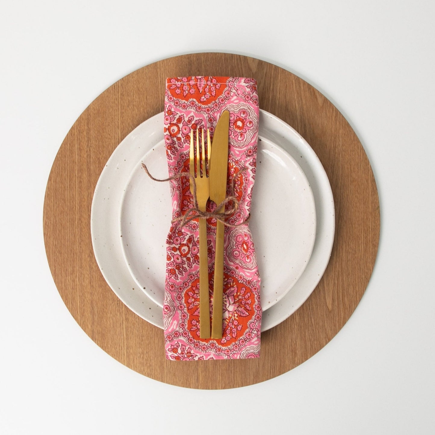 floral napkin tied with string sitting on white plate with gold cutlery