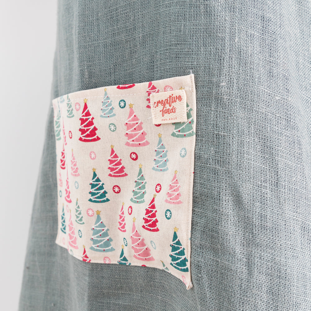 
                  
                    close up of pocket on green linen apron with christmas fabric on pocket and frill
                  
                