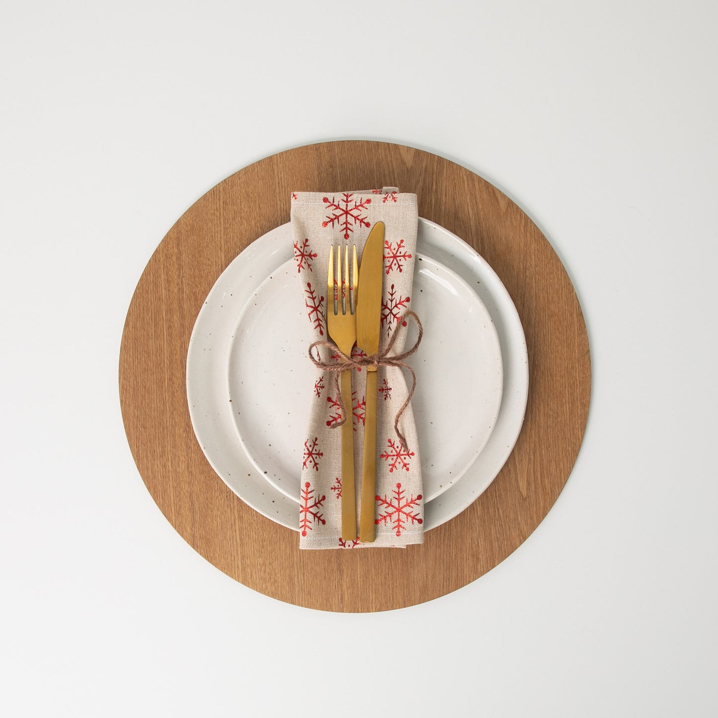 
                  
                    Christmas Snowflake Napkin tied with string and gold cutlery on white plate sitting on placemat
                  
                